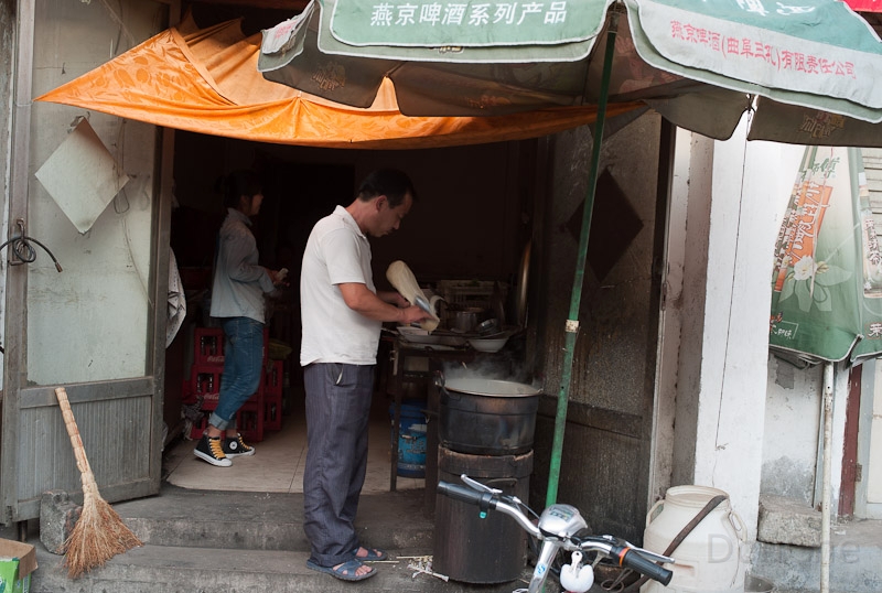 L1009871.jpg - Making a noodle soup ... the white thing in the hands is dough, which is peeled of in small stripes with a knife that fall into the soup ...